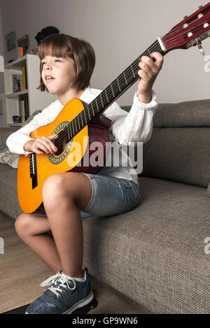 Little girl playing guitar sitting on the sofa at home Stock Photo