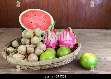 Asian fresh fruits. Langsat and watermelon and Orange and Dragon fruit in bamboo basket. Stock Photo
