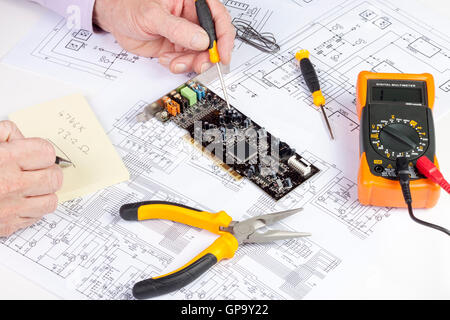 Electronics engineer writing on a pad the results from his computer circuit testing Stock Photo