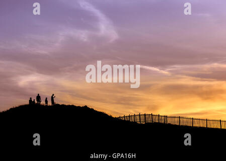Holidaymakers in silhouette watch a spectacular sunset break over Porth Island in Newquay, Cornwall. Stock Photo