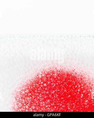 Red ink flowing through soap suds, closeup. Stock Photo