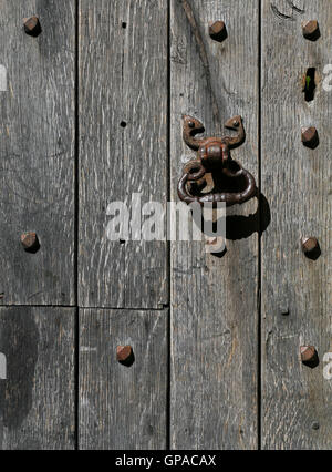 Old rusty metal door knocker on a medieval style aged oak timber door with rivets background Stock Photo