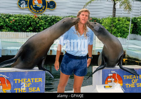 A female animal trainer gets wet kisses from two California sea lions that she teaches to perform in aquatic shows for visitors at the Theater of the Sea, a marine mammal park in Islamorada, Florida, USA. Its 17 acres (6.9 hectares) of lagoons and tropical gardens also are home to Atlantic bottlenose dolphins, sea turtles, sharks, stingrays, alligators, game fish and many birds. This popular tourist attraction in the Florida Keys has been family owned and operated since 1946. Stock Photo