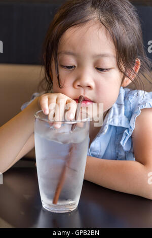 Child using straw to drink cold water from glass. Stock Photo