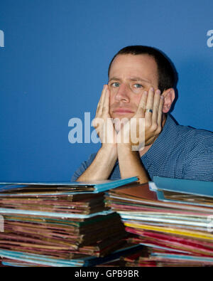 Young man at desk with hands on his cheeks stressed out by all the files in front of him. Stock Photo