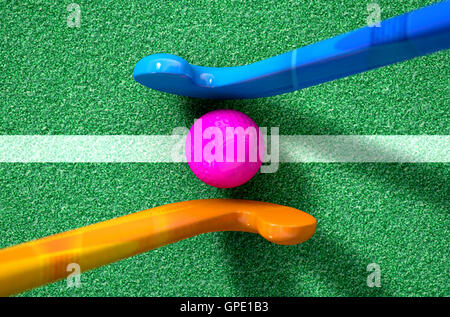 A 3D rendering of two hockey sticks standing opposite each other over a ball on green astro turf in the daytime Stock Photo