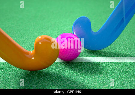 A 3D rendering of two hockey sticks standing opposite each other over a ball on green astro turf in the daytime Stock Photo