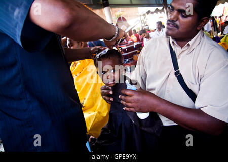 A young girl cries as she has her head shaved at the Thaipusam festival, Batu Caves, Malaysia. Stock Photo