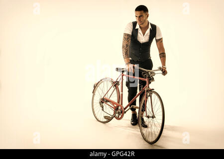 Portrait of young tattooed man in elegant clothes and shoes riding a bicycle. Studio shot. Full body shot Stock Photo