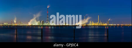Panoramic view over the Scheldt river in Antwerp, Belgium to a large oil refinery with night blue sky, illumination and steam. Stock Photo