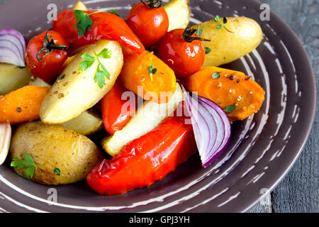 Rustic oven baked vegetables (potato, tomato, carrot, pepper, onion) with spices and herbs on plate close up, vegetarian organic Stock Photo