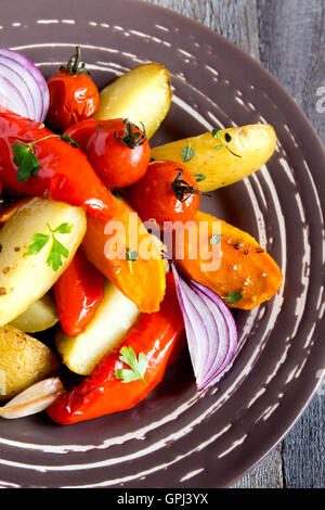 Rustic oven baked vegetables (potato, tomato, carrot, pepper, onion) with spices and herbs on plate close up, vegetarian organic Stock Photo