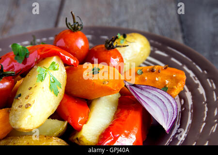 Rustic oven baked vegetables (potato, tomato, carrot, pepper, onion) with spices and herbs on plate close up, vegetarian organic Stock Photo