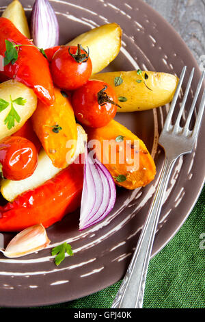 Rustic oven baked vegetables (potato, tomato, carrot, pepper, onion) with spices and herbs on plate close up, vegetarian organic Stock Photo