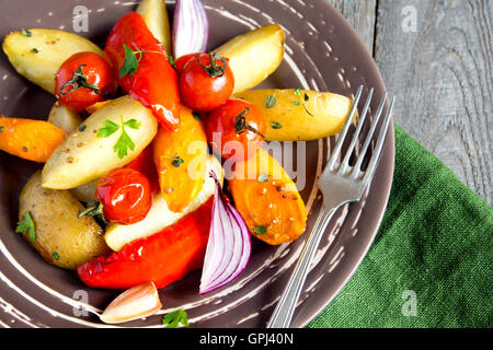 Rustic oven baked vegetables (potato, tomato, carrot, pepper, onion) with spices and herbs on plate close up, vegetarian organic Stock Photo