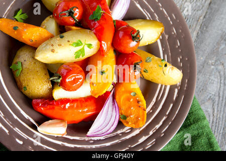 Rustic oven baked vegetables (potato, tomato, carrot, pepper, onion) with spices and herbs on plate close up, vegetarian organic Stock Photo
