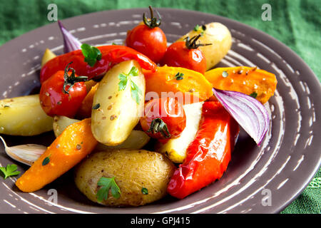 Rustic oven baked vegetables (potato, tomato, carrot, pepper, onion) with spices and herbs on plate close up, vegetarian organic Stock Photo