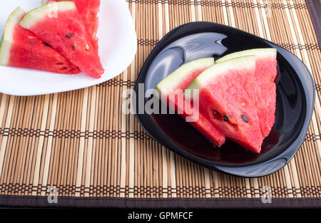 Chunks of juicy red watermelon on black and white plate on a bamboo mat closeup with shallow depth of focus Stock Photo