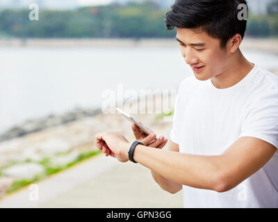 young asian man using apps in smartphone and smartwatch to track fitness data during exercise Stock Photo