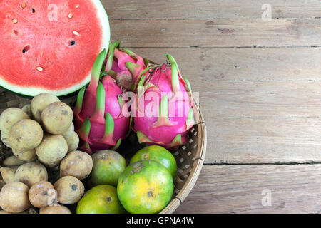 Asian fresh fruits. Langsat and watermelon and Orange and Dragon fruit in bamboo basket. Stock Photo