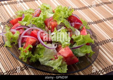 View angle on a fragment of vegetarian salad from fresh vegetables closeup at the plate on a bamboo mat tabletop Stock Photo