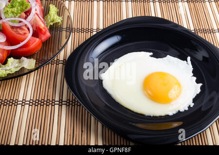 Close-up top view on a black plate with a fried egg and yolk on striped mat. Stock Photo