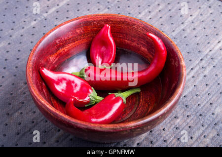 View close-up on hot red chili peppers in a brown wooden bowl on a fabric background Stock Photo