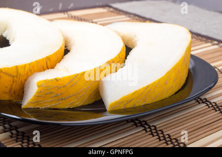 Three slices of juicy yellow melon on a black plate closeup on wooden background Stock Photo