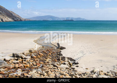 A small stream leads the eye through a sandy beach to beautiful turquoise waters on a mostly clear and sunny day. Stock Photo