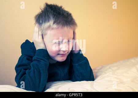 Sad tired worried unhappy kid (boy, teen) with eyes closed covering ears with hands, portrait with copy space Stock Photo