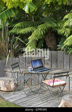 Working from home: a laptop computer, smart phone and coffee mug on a garden table in an urban, UK garden on a summer day. Stock Photo