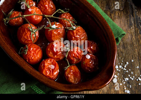 Rustic oven baked tomatoes with olive oil and sea salt in ceramic dish over dark wooden background Stock Photo