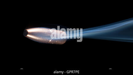 Bullet with copper plating and smoke behind with a black background ...