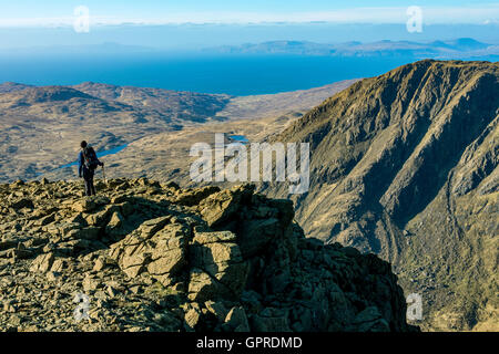 A walker on the summit ridge of Trollabhal in the Rum Cuillin hills, Isle of Rum, Scotland, UK. Isle of Skye in the distance. Stock Photo