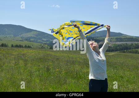 Woman holding yellow and blue scarf which is waving on wind in landscape Stock Photo
