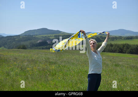 Woman holding yellow and blue scarf which is waving on wind in landscape Stock Photo