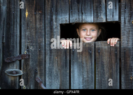 Little girl peeking through a crack in a wooden shed. Stock Photo