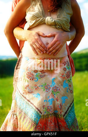 Loving beautiful ethno couple, man makes the heart shape on her pregnant belly. Stock Photo