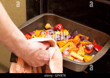 Home cooking. Person taking a tray of roasted vegetables from an oven Stock Photo