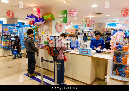 Interior of the gift shop at the Osaka Aquarium, Kaiyukan. Man, looking down as he takes money from his wallet while being served by woman cashier Stock Photo