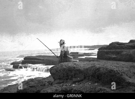 1930s, historical, Sidney H.Smith sitting on coastal rocks at low tide fishing at Filey Brigg, a promontory, North Yorkshire, England. Stock Photo