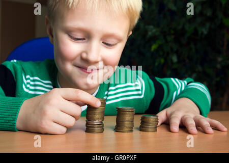 Happy child (boy, kid, teen) making stacks of coins on the table. Children and money concept. Stock Photo