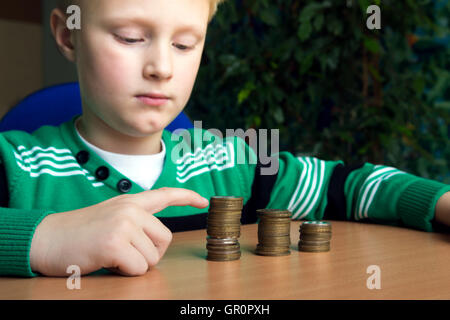 Happy child (boy, kid, teen) making stacks of coins on the table. Children and money concept. Stock Photo