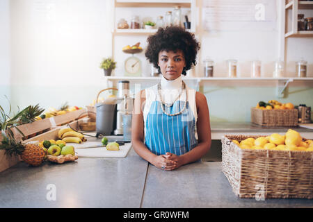 Portrait of young african woman wearing apron standing behind juice bar counter looking at camera. Stock Photo