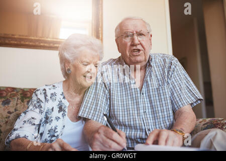 Portrait of a elderly couple signing documents while sitting at home. Senior caucasian man and woman sitting on sofa and signing Stock Photo
