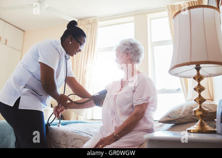 Female nurse doing blood pressure measurement of a senior woman patient. Doctor checking blood pressure of an elderly woman at o Stock Photo