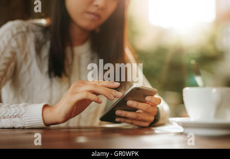 Young asian woman sitting at a table using mobile phone. Smart phone in hands of a female at outdoor cafe. Stock Photo