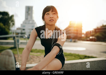 Fit woman stretching her legs before training session. Beautiful chinese athlete exercising outdoors in city park. Stock Photo