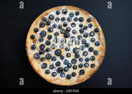 Homemade blueberry pie on black wooden plate. Delicious pastry with fresh berries, cream and sugar. Flat lay overhead shot. Stock Photo