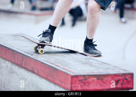 Skater boy grinding on a ledge in outdoor skate park. Popular extreme sport, dangerous, fun. Focus on skateboard Stock Photo